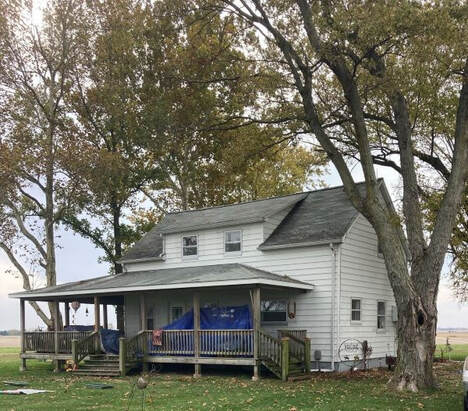 Picture of a farm house before painting. You can see worn out white paint on the house.